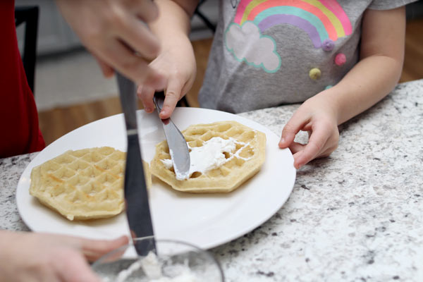 Children spreading cream cheese on a waffle