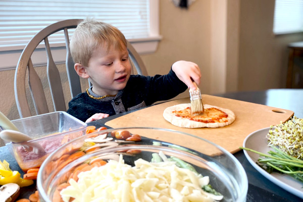 Preschooler spreading sauce on crust