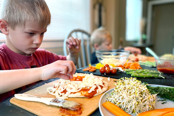 Young boy adding toppings to his veggie pizza
