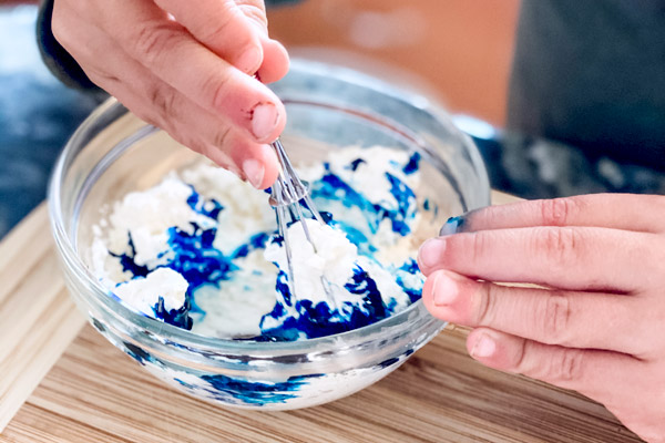 Small child adding blue food coloring to cream cheese