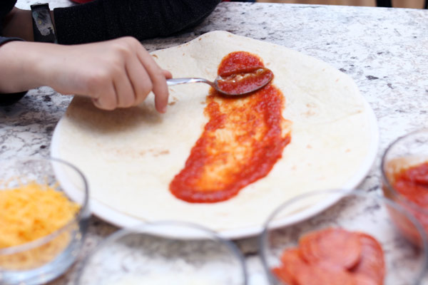 Child spreading pizza sauce on tortilla
