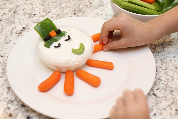 Child placing hat made of bell pepper into dip