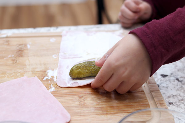 Child wrapping pickle inside ham roll