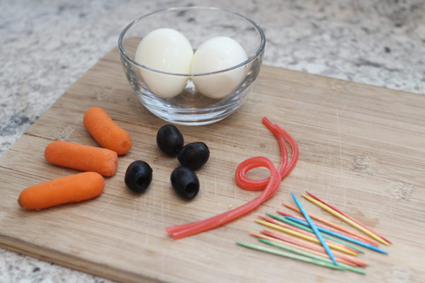 Eggs, carrots, olives, toothpicks, and licorice string on a cutting board