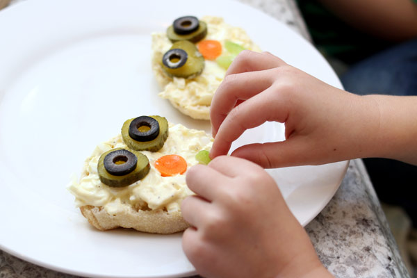 Child adding a face to the sandwich with veggies