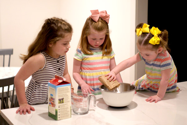 Little girls adding pudding mix to bowl