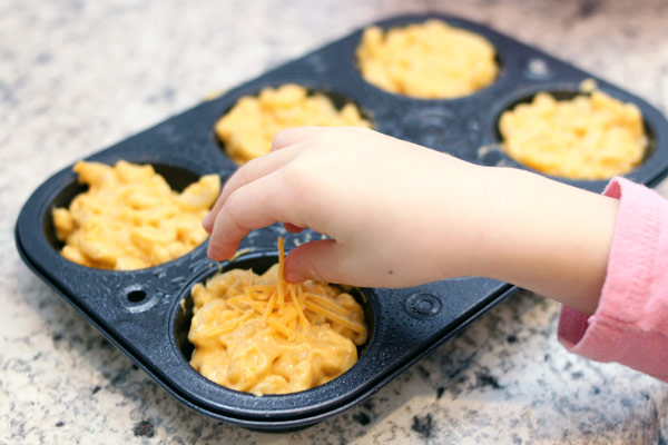 Preschooler topping mac and cheese with shredded cheese