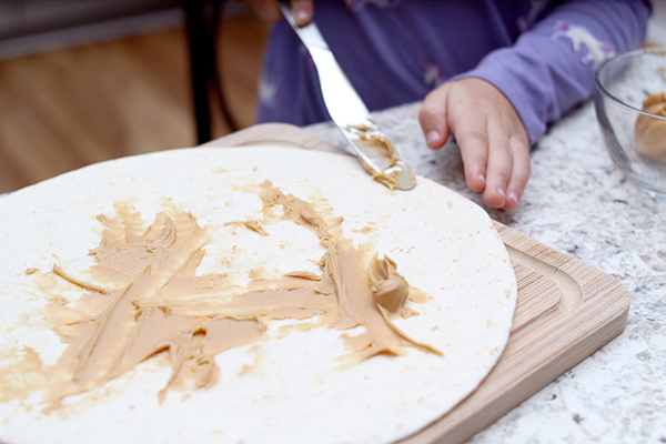 Child spreading peanut butter on a tortilla