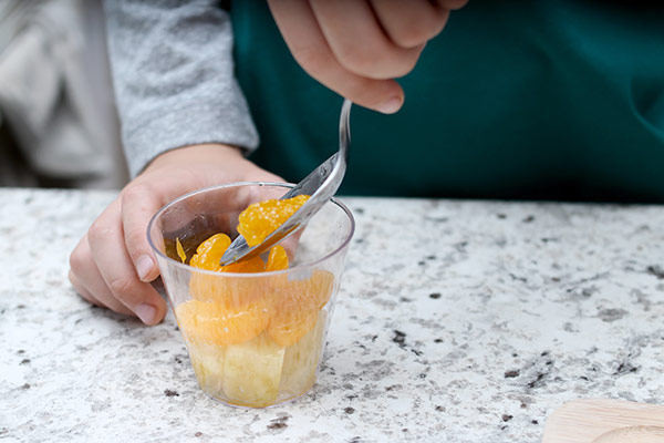 Child spooning pineapple chunks into a cup