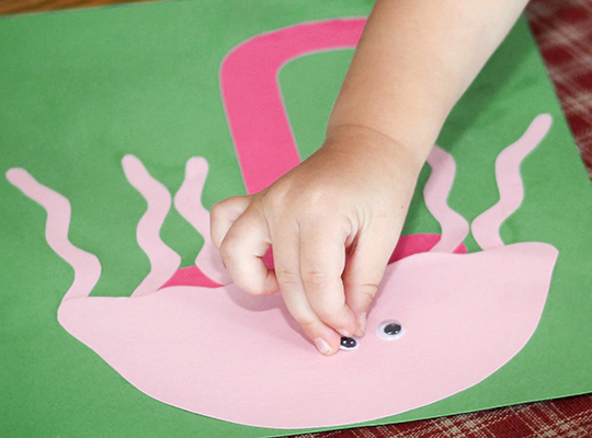 child gluing an eye to her letter j craft