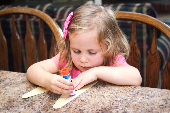 child putting glue on her letter m craft