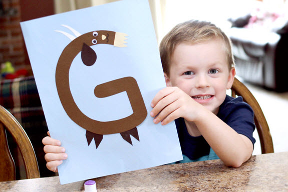 little boy holding up his finished letter G craft