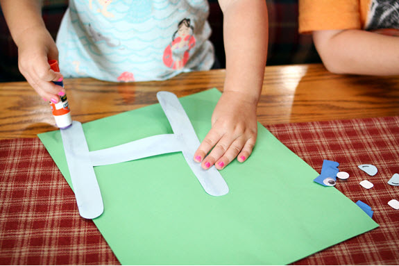 child adding glue to her letter h craft