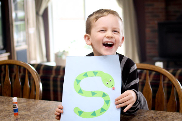 laughing boy holding up his finished letter s craft