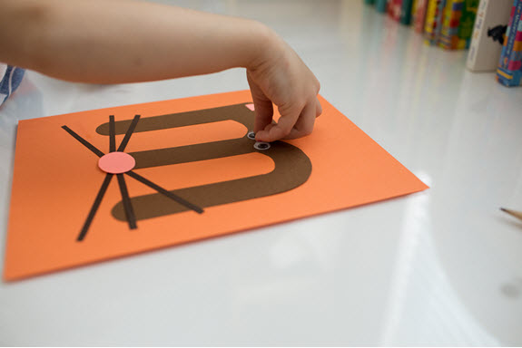 child glues an eye to her uppercase letter M craft