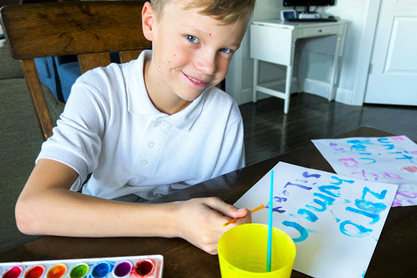 boy writing words on paper with water color paints