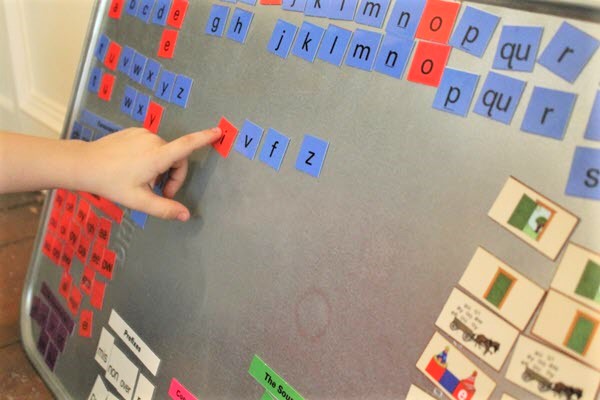 child's hand works with letter tiles arranged on a metal pan