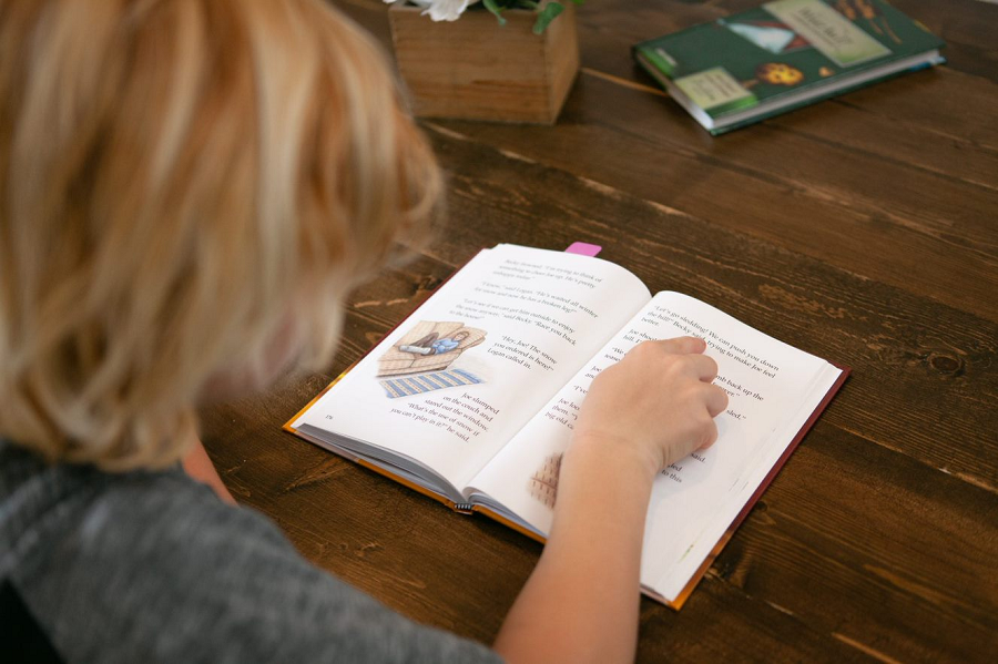 A young boy independently reads from an open book from All About Reading Level 3.