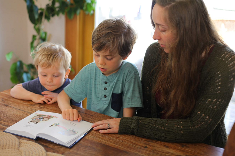 A mother using an All About Reading reader with her two young ESL children