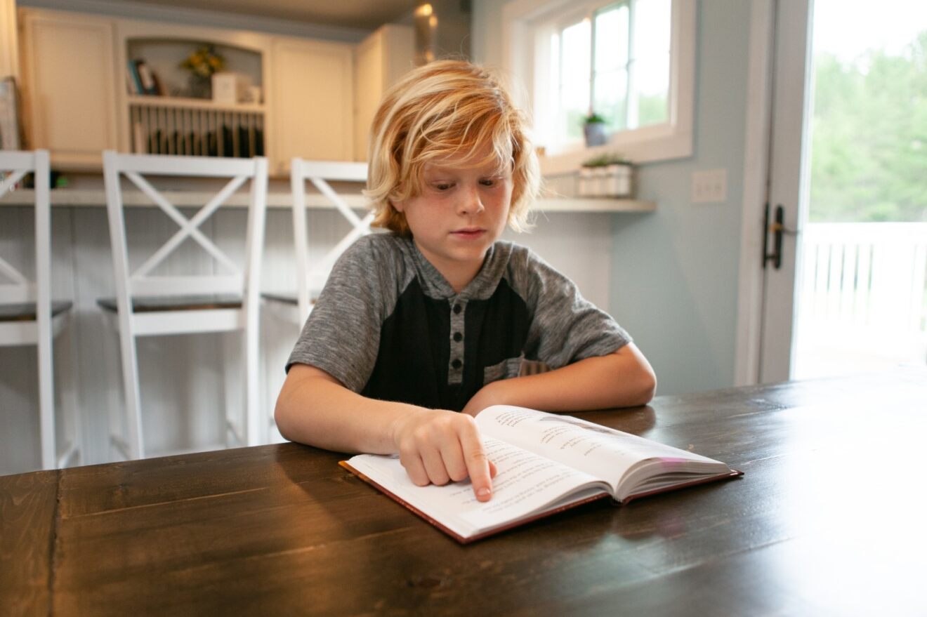 a boy reading a book with his finger on the page helping him read
