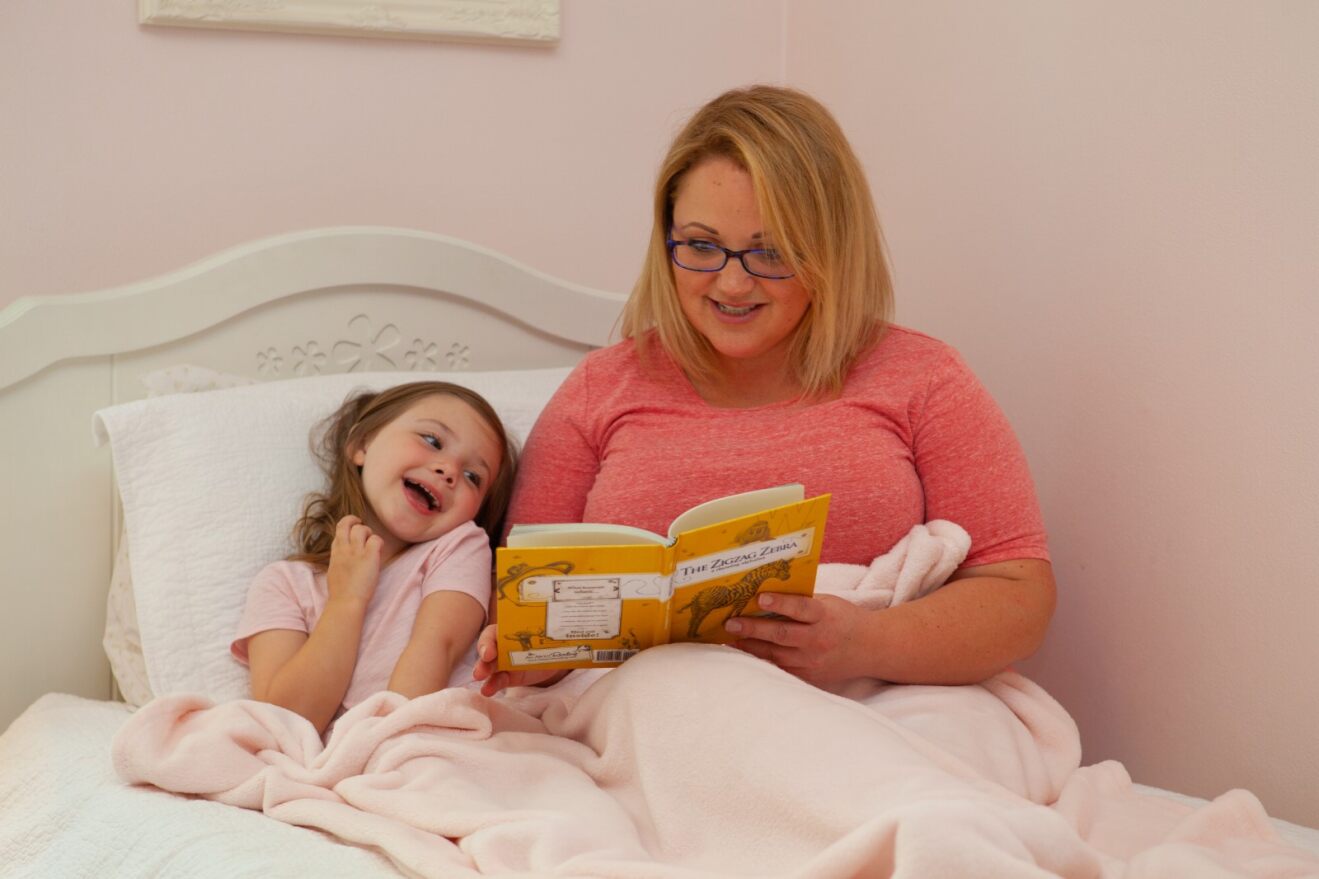 a young girl reading in bed with her mom