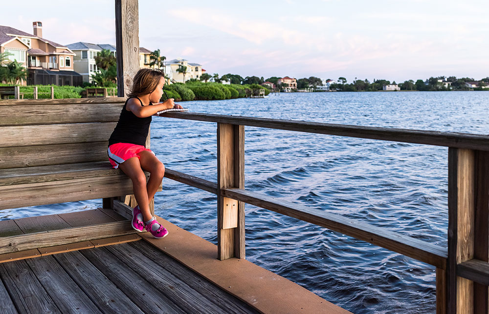 A girl sits on a wooden bench and looks out across a lake