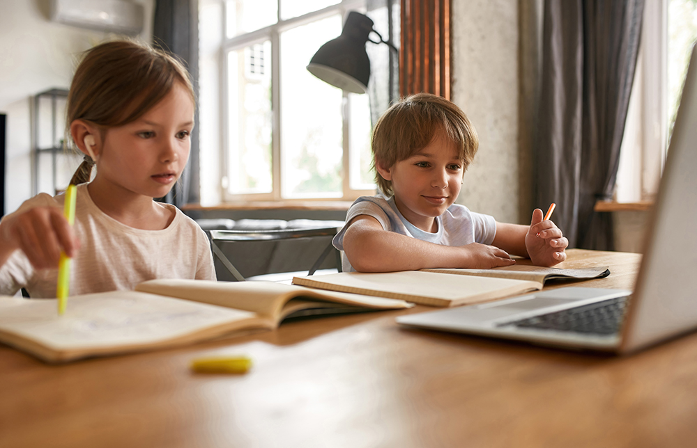 A boy and a girl sitting at a table and doing homeschool work together